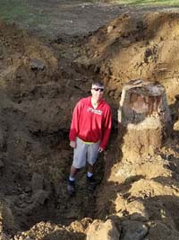 Bob Whyte posing with excavation and stump removal before construction of customized tan and green backyard basketball court in Londonderry, New Hampshire.
