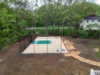 Overview from side, before landscaping, of sand and green backyard basketball court with custiom team logos and text in Londonderry, NH.