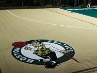 Closeup of custom Celtics logo on corner of sand and green backyard basketball multicourt in Londonderry, NH.