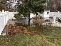 Flooding in poorly drained area of yard that will host a royal blue and yellow basketball court and accessories in Stoneham, MA.