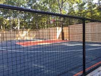 View through mesh fence at graphite and orange backyard basketball court with custom fence that incorporates more traditional wood in Walpole, MA.