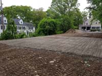 Area cleared and gravel/sand packed to build foundation for black and grey home backyard basketball court in Wellesley, MA.